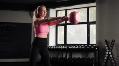 Attractive young beautiful woman doing cardio exercise and squatting with kettlebell in gym