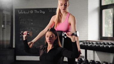 Female coach trainer trains girl during shoulder exercise with dumbbells