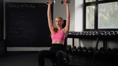 The girl does an exercise in gym. Female athletic woman exercising shoulders with dumbbells