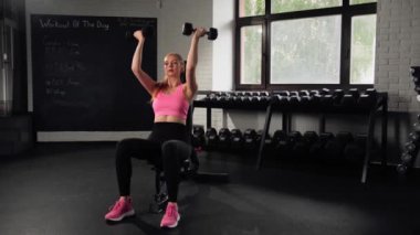 The girl does an exercise in gym. Female athletic woman exercising shoulders with dumbbells
