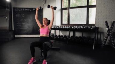 The girl does an exercise in gym. Female athletic woman exercising shoulders with dumbbells