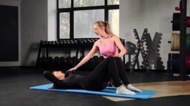 Coach woman training girl during abs exercise in gym