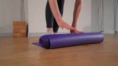 Woman rolling up yoga mat after training in studio. Girl folding fitness mat on floor at yoga studio
