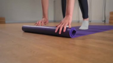 Woman rolling up yoga mat after training in studio. Girl folding fitness mat on floor at yoga studio