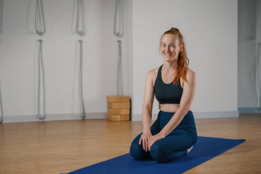 Woman smiling at camera while sitting on yoga mat during Pilates stretching class in the studio.