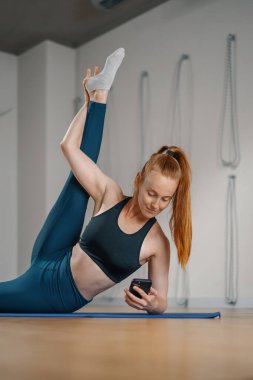 Athletic woman texting on the phone while doing stretching pilates yoga for health in studio. athletic body girl