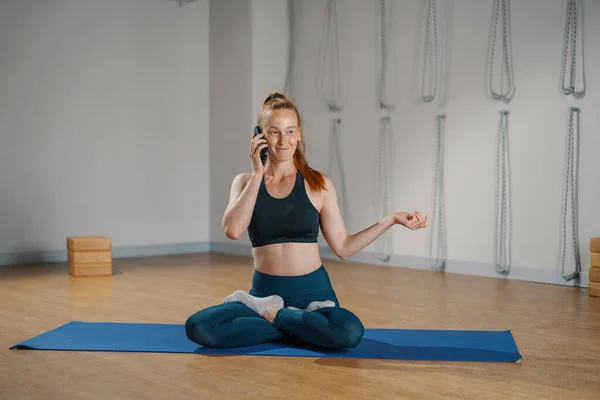 Athletic woman talking on the phone while doing pilates yoga stretching for health in studio. athletic body girl