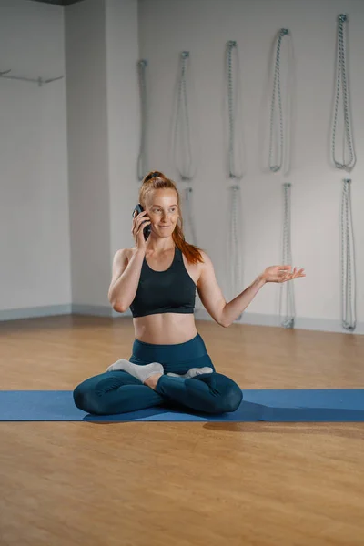 Athletic woman talking on the phone while doing pilates yoga stretching for health in studio. athletic body girl