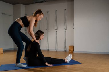 Athletic physique female coach conducts a yoga pilates stretching workout in studio for client. Trains a girl..