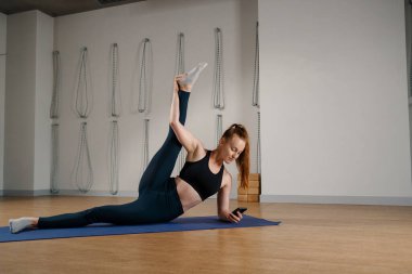 Athletic woman texting on the phone while doing stretching pilates yoga for health in studio. athletic body girl