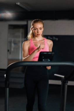 Athletic build girl doing cardio training exercise by jogging on a treadmill in gym