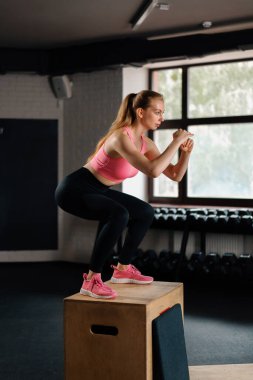 Athletic build girl doing a workout exercise by jumping on wooden box. Workout with sports equipment