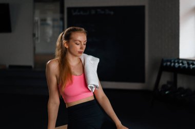 Athletic girl wipes sweat while relaxing after a grueling workout in gym