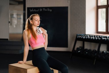 Athletic girl wipes sweat while relaxing after a grueling workout in gym