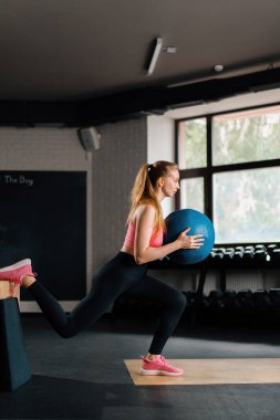 athletic girl doing workout exercise lunges with a ball in gym