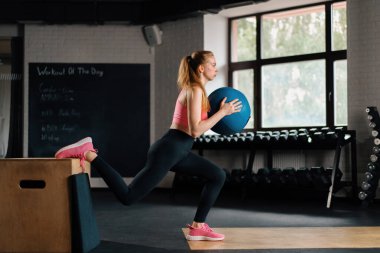 athletic girl doing workout exercise lunges with a ball in gym