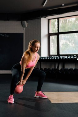 Athletic woman doing squat mobility workout exercise with kettlebell.