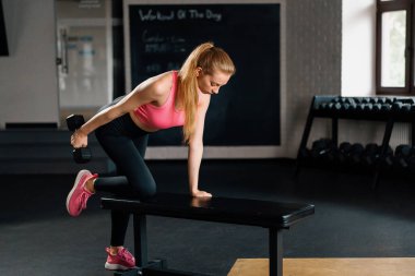 Athletic woman doing dumbbell traction in the gym. back workout.