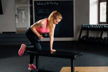 Athletic woman doing dumbbell traction in the gym. back workout.
