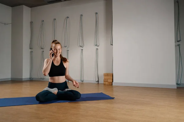 Athletic woman talking on the phone while doing pilates yoga stretching for health in studio. athletic body girl