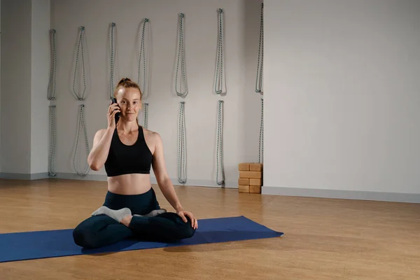 Athletic woman talking on the phone while doing pilates yoga stretching for health in studio. athletic body girl