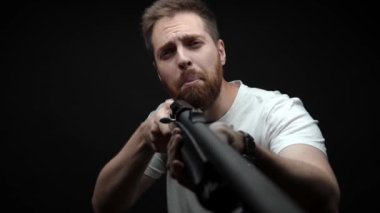 Close-up: a man holds a shotgun in his hands and aims looks at camera