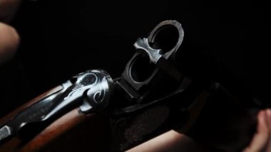 Close-up: a man in a black T-shirt on a black background loads shotgun