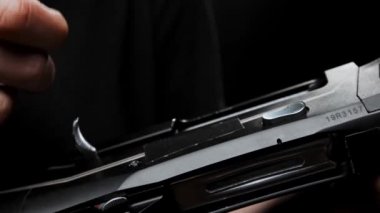 Close-up: a man in a black T-shirt on a black background loads shotgun