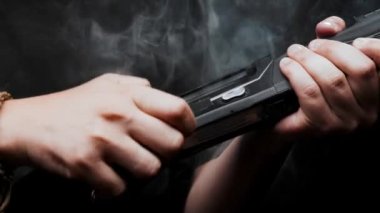 Close-up: a man in a black T-shirt on a black background loads shotgun