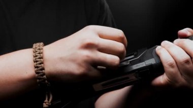 Close-up: a man in a black T-shirt on a black background loads shotgun