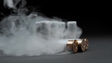Close-up of a man picking up shotgun shells from a table against dark background