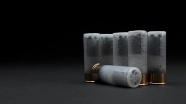 Close-up: Shotgun shells are on the table against a dark background, one cartridge is rolled into frame