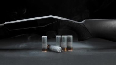 Close-up: smoke slides down a hunting shotgun with cartridges on table against a dark background