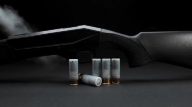 Close-up: smoke slides down a hunting shotgun with cartridges on table against a dark background
