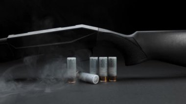 Close-up: smoke slides down a hunting shotgun with cartridges on table against a dark background