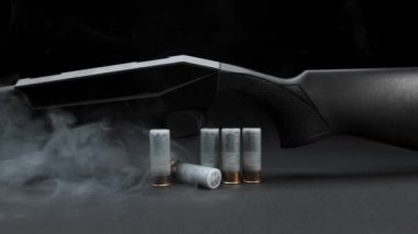 Close-up: smoke slides down a hunting shotgun with cartridges on table against a dark background