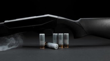 Close-up: smoke slides down a hunting shotgun with cartridges on table against a dark background