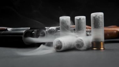Close-up of a loaded shotgun after being fired and cartridges on table in smoke