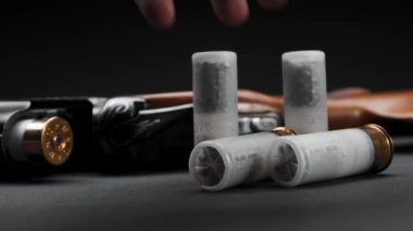Close-up: loaded shotgun and cartridges on the table, the man takes cartridge