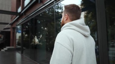 A bearded man with a serious face walks near the business center, looks at camera with serious face
