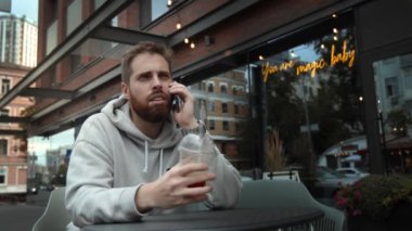 Attractive young man with a beard is talking on the phone on a work issue and drinking coffee on a date with woman.