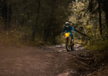 Ormandaki profesyonel motosiklet sürücüsü doğa yolundaki çamurdan geçer..