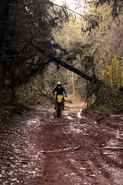 Ormandaki profesyonel motosiklet sürücüsü doğa yolundaki çamurdan geçer..