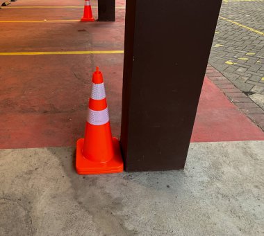 Kullanılmayan trafik konisi otoparkta, bina desteğinin yanında.