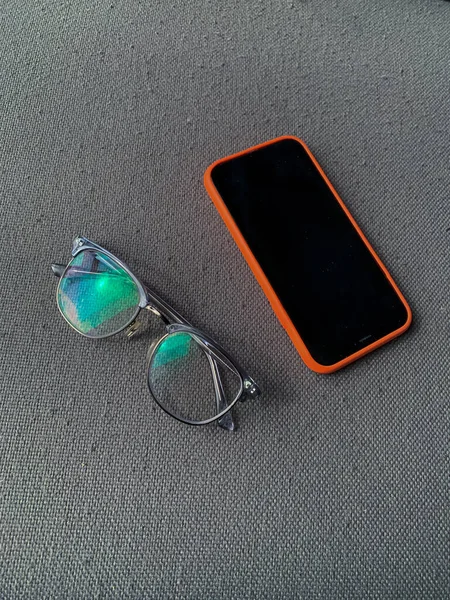 Frauenbrille Neben Smartphone Mit Orangefarbener Hülle Auf Grauem Sofa — Stockfoto