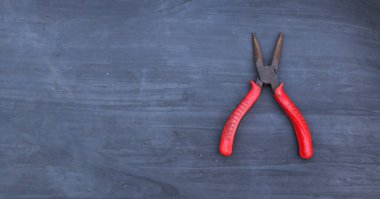 Gri arka planda kırmızı saplı pense.