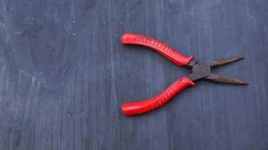 Gri arka planda kırmızı saplı pense.