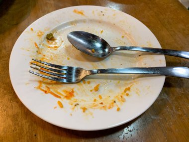 Kirli kaşığı ve çatalı olan beyaz bir tabak. Çünkü az önce restoranda yemek yemek için kullanıldı.