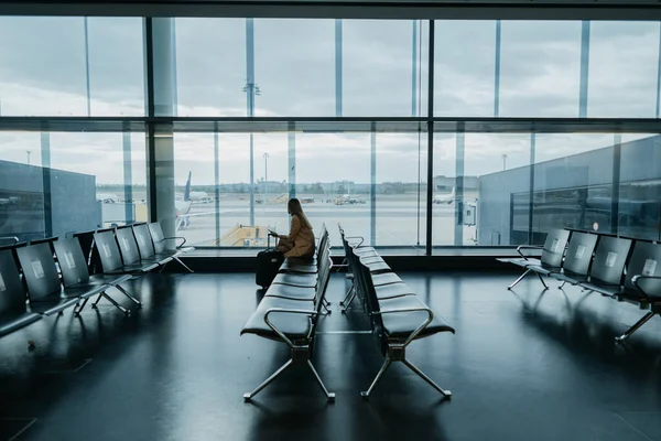 Boş havaalanı salonunda oturan genç bir kadın. Uçuşu bekliyorum. Kopyalama alanı