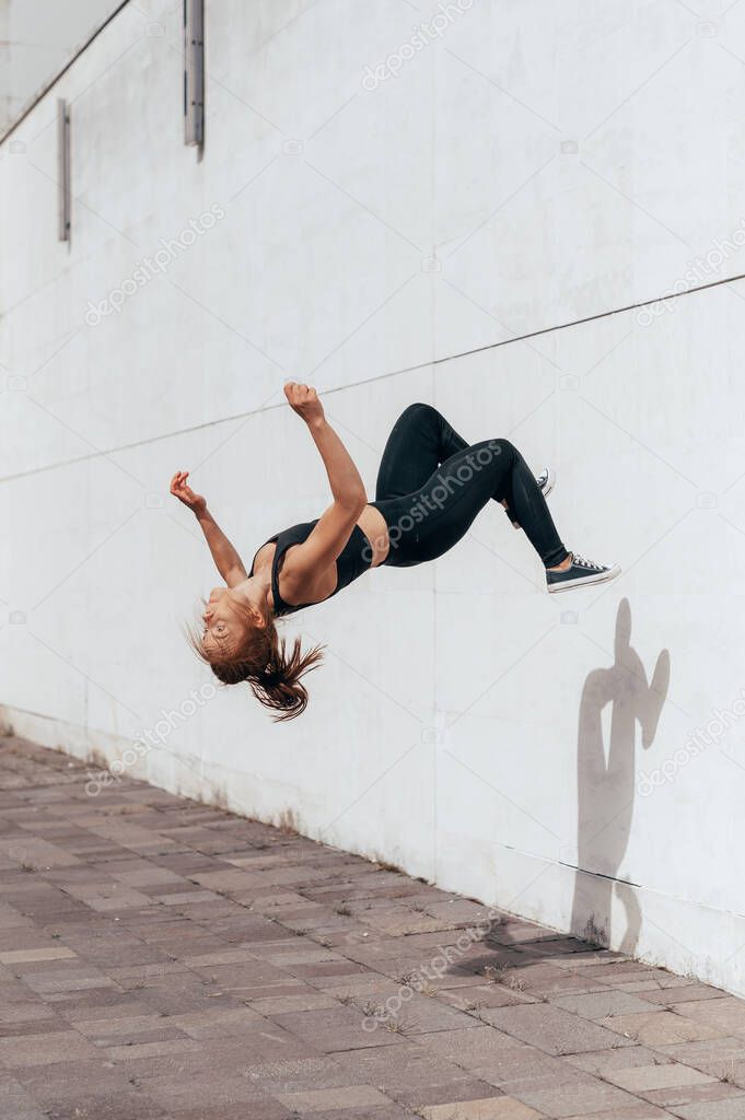 Girl doing parkour backflip on the urban place. Sport lifestyle women doing acrobat trick in the city. vertical photo